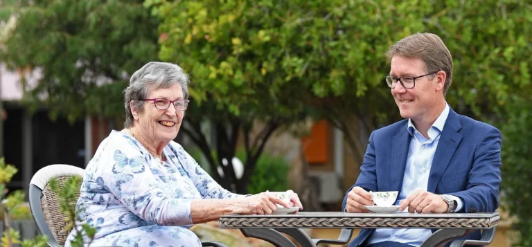 An older woman and a middle-aged man sat at a table, smiling and nursing a cup of tea.